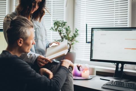 Man and woman both looking at a notepad infront of a computer screen