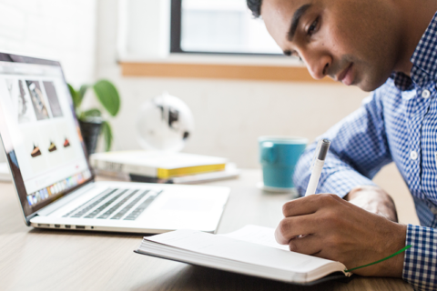 Man writing notes in front of a laptop