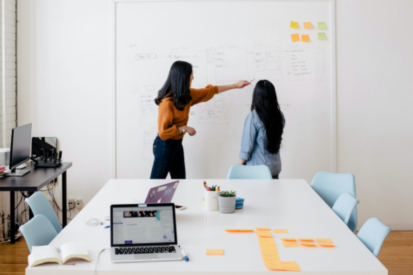 two women standing next to each other working on a whiteboard