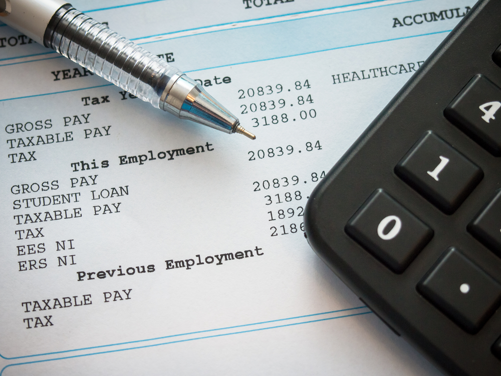 payslip placed underneath a calculator and pen